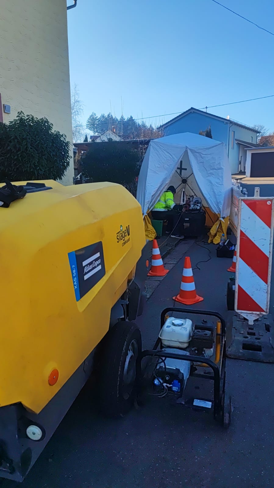Zona de trabajo en calle con carpa de empalmes, compresor y conos de señalización.
