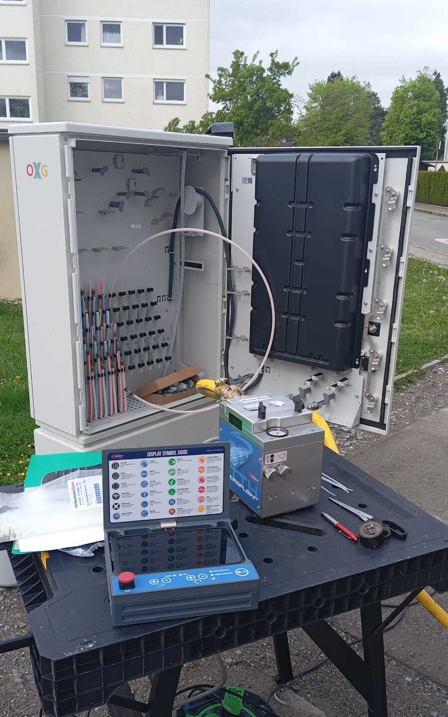 Armario de fibra óptica abierto con equipos de empalme y medición sobre la mesa de trabajo.